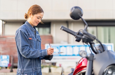 バイクの前で書類を書いている女性の画像