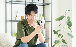 悩んだ様子で携帯を見ている男性の画像