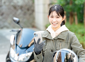 女性ライダーがバイクの前で携帯とヘルメットを持っている写真